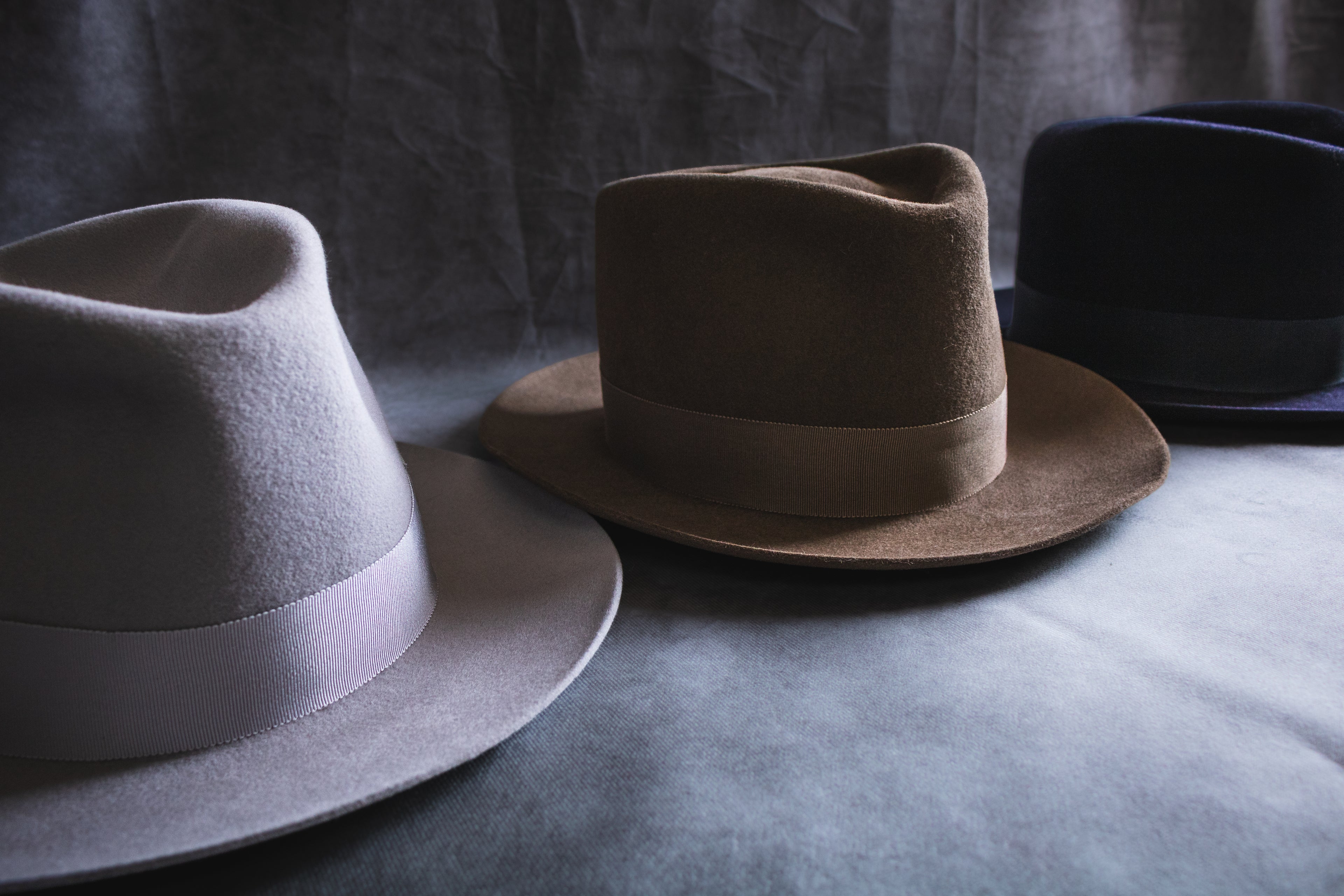 Three hats in gray, brown, and black on a textured surface with a neutral background.